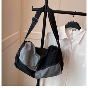 Detail of a large denim crossbody tote bag with adjustable black strap hung in a room