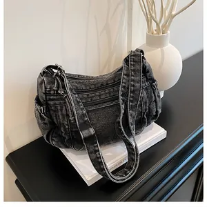 Detail of black denim hobo bag featuring multiple functional zippers and vintage wash texture