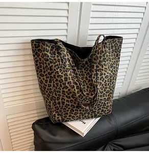 Close-up of leopard print canvas tote bag with metal logo detail on a black sofa