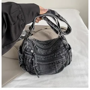 Detail of dark washed denim hobo bag featuring triple front zippers and side ruched pocket