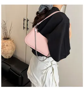 Detail of pink woven shoulder bag with silver chain worn by model in minimalist home setting