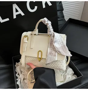 Detail of off-white woven handbag with gold U-lock and decorative floral scarf on handle
