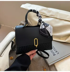 Detail of black woven leather handbag with gold oval lock and floral scarf on handle