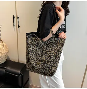 Close-up of a large leopard print canvas tote bag featuring an oval metal logo plaque