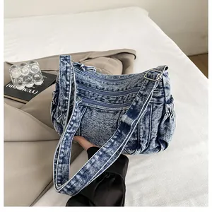 Detail of blue acid wash denim crossbody bag featuring multiple zippers and side pockets