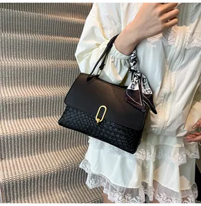 Detail of black bag featuring woven texture and a gold oval clasp with silk scarf accent