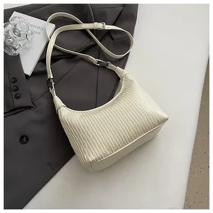 Detail der cremefarbenen Falten-Handtasche mit Silberschnalle auf grauem Blazer-Hintergrund