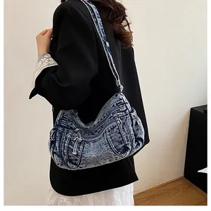 Side view of blue washed denim dumpling bag with drawstring and zipper details