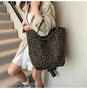 Detail of large leopard print tote bag with golden metal logo plaque and canvas texture