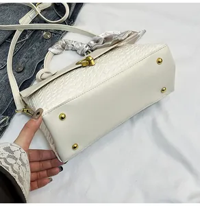 Detail of cream woven handbag with gold base studs and a silk scarf wrapped handle