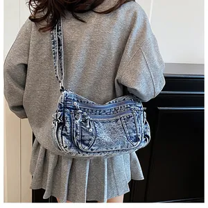 Detail of blue denim crossbody bag with multiple zippers and pockets on a model
