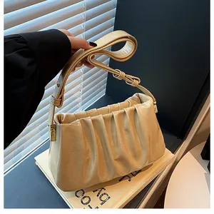 Detail view of cream pleated handbag with adjustable strap and gold metal hardware