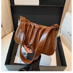 Close-up of brown pleated PU leather bag with shiny texture and golden metal buckle