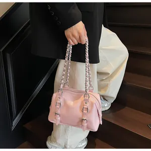 Close-up of pink Boston bag with metallic chain strap and decorative buckles on stairs