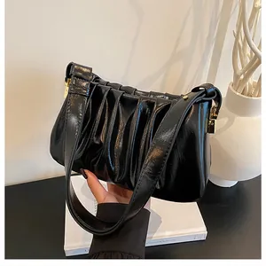 Detailed close-up of black pleated cloud shoulder bag with gold hardware buckle and wide strap