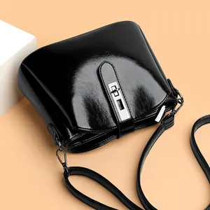 Retro black glossy leather shoulder bag with silver metal lock on a pink background
