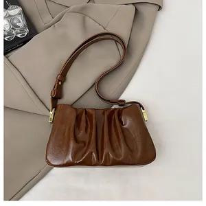 Detail of dark brown ruched shoulder bag with glossy texture and gold hardware accents