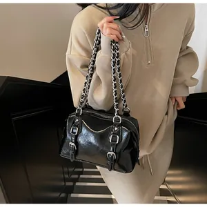 Detail of high-gloss black shoulder bag featuring silver buckle and chain strap on model