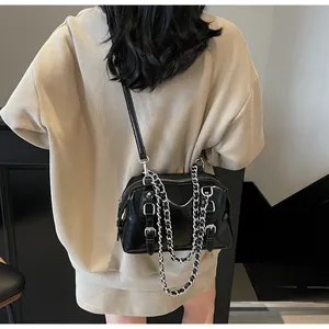 Detail view of black patent leather crossbody bag with silver chain and buckle accents