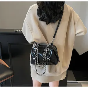 Detail of black glossy crossbody bag with silver chains on a casual knit sweater