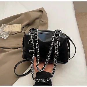 Detail of glossy black leather handbag featuring thick silver chain and metal buckle