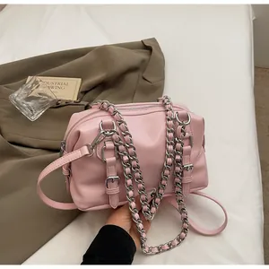 Detail of pink Boston bag with silver chain strap and leather belt accents on white background