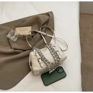 Detail of a creamy white leather handbag featuring a chunky silver chain and buckle straps