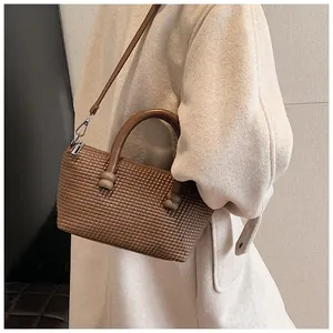 Gros plan d'un sac à main marron tissé avec manteau en laine beige et détail de poignée sphérique