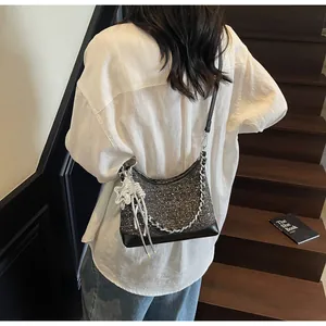 Detail of black tweed hobo bag with silver star charm worn by a model on wooden stairs