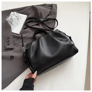 Detail of black pleated lychee grain leather crossbody bag on a gray suit background