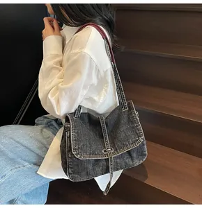 Close-up of vintage denim tote bag with leather strap on a model sitting on wooden stairs