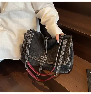 Detail of vintage denim tote bag featuring red leather handles and metal buckle accents