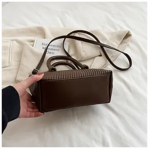 Détail d'un sac à main marron foncé à texture tissée avec base en cuir et bandoulière