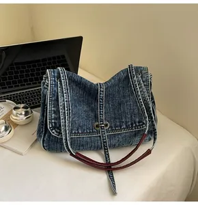 Detail of blue denim tote bag featuring vintage metal buckle and burgundy leather handle