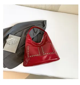 Detail of red patent leather tote bag with silver hexagonal rivets on white background