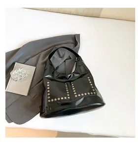 Detail of glossy black tote bag with silver hexagonal rivets on industrial style hobo bag