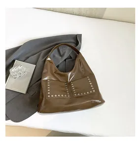 Detail of dark brown glossy tote bag featuring silver hexagonal rivets and front pockets