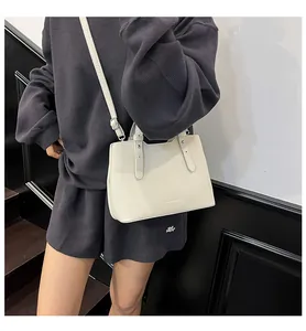 Dettaglio della borsa a tracolla minimalista in pelle beige indossata con abito grigio