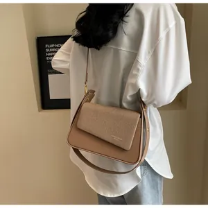 Détail du sac à bandoulière chameau avec rabat tissé sur un mannequin au style minimaliste