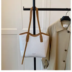 Detail of a woven tote bag with brown leather straps hanging next to a khaki trench coat