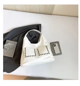 Close-up of white hobo bag with studded pockets and wide strap on a minimalist desk