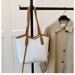 Detail of white woven tote bag with brown leather handles and fashion logo on the front
