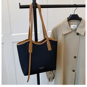 Detail of black textured tote bag with brown leather handles hanging next to a trench coat
