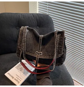 Detail of dark denim tote bag featuring silver metal buckle and red leather strap stitching
