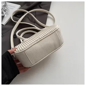 Close-up of cream-colored crossbody bag featuring pebbled leather and elegant ruched sides