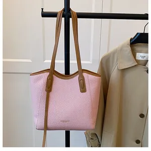 Detail of pink woven tote bag with brown leather handles and fashion logo text