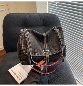 Detail of dark wash denim tote bag with brown leather strap and silver metal buckle
