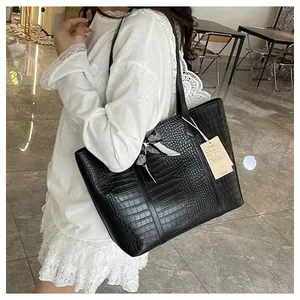 Détail du sac cabas noir à motif crocodile avec nœud à carreaux et étiquette produit