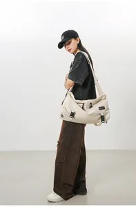 Dettaglio della borsa a tracolla in tela beige con fibbie nere e etichetta del marchio