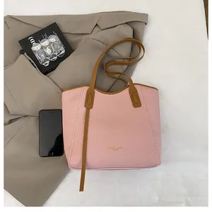 Detail of pink woven tote bag featuring dark brown leather straps and gold foil logo